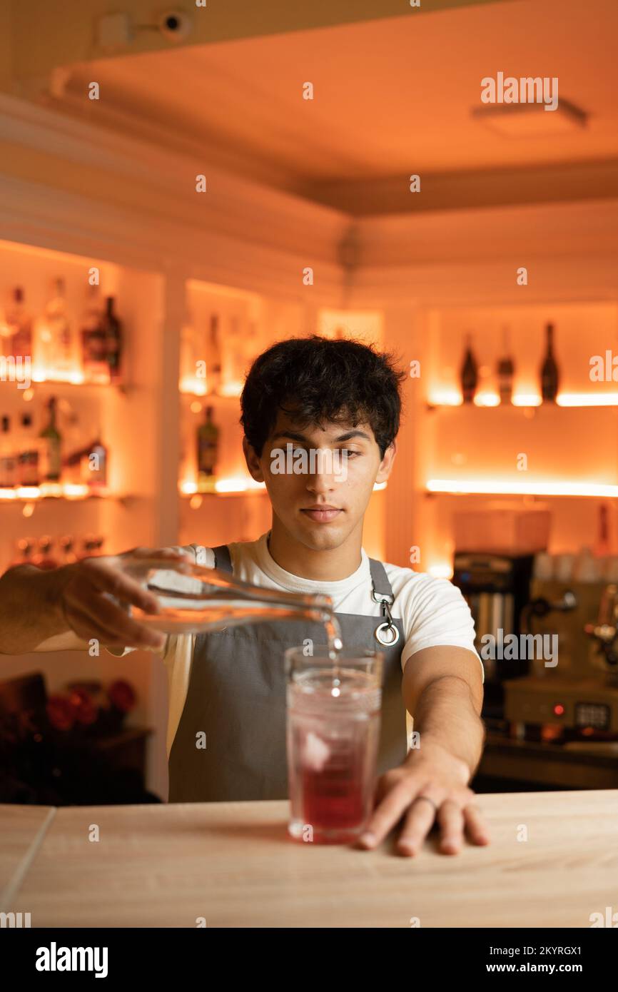 Bartender pouring tonic water in alcoholic cocktail in glass on bar