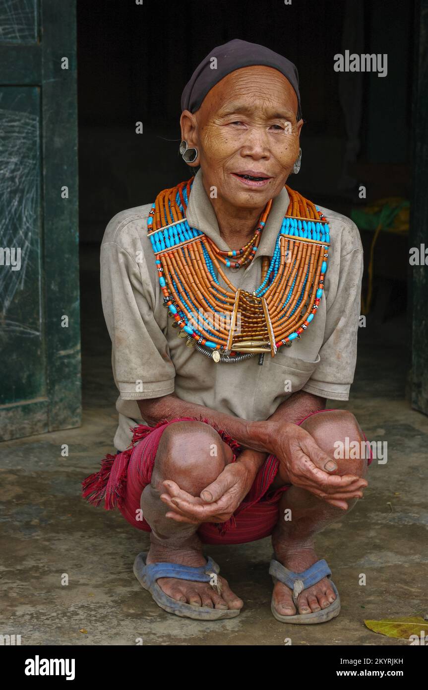Mon, Nagaland, India - 03 03 2009 : Portrait of old Naga Konyak tribe woman squatting, wearing traditional necklace and earrings with black head scarf Stock Photo