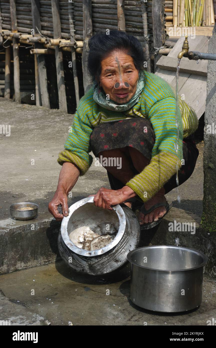 Ziro, Arunachal Pradesh, India - 03 04 2014 : Portrait of Apatani tribal woman with traditional facial tattoos and nose plugs washing cooking pots Stock Photo