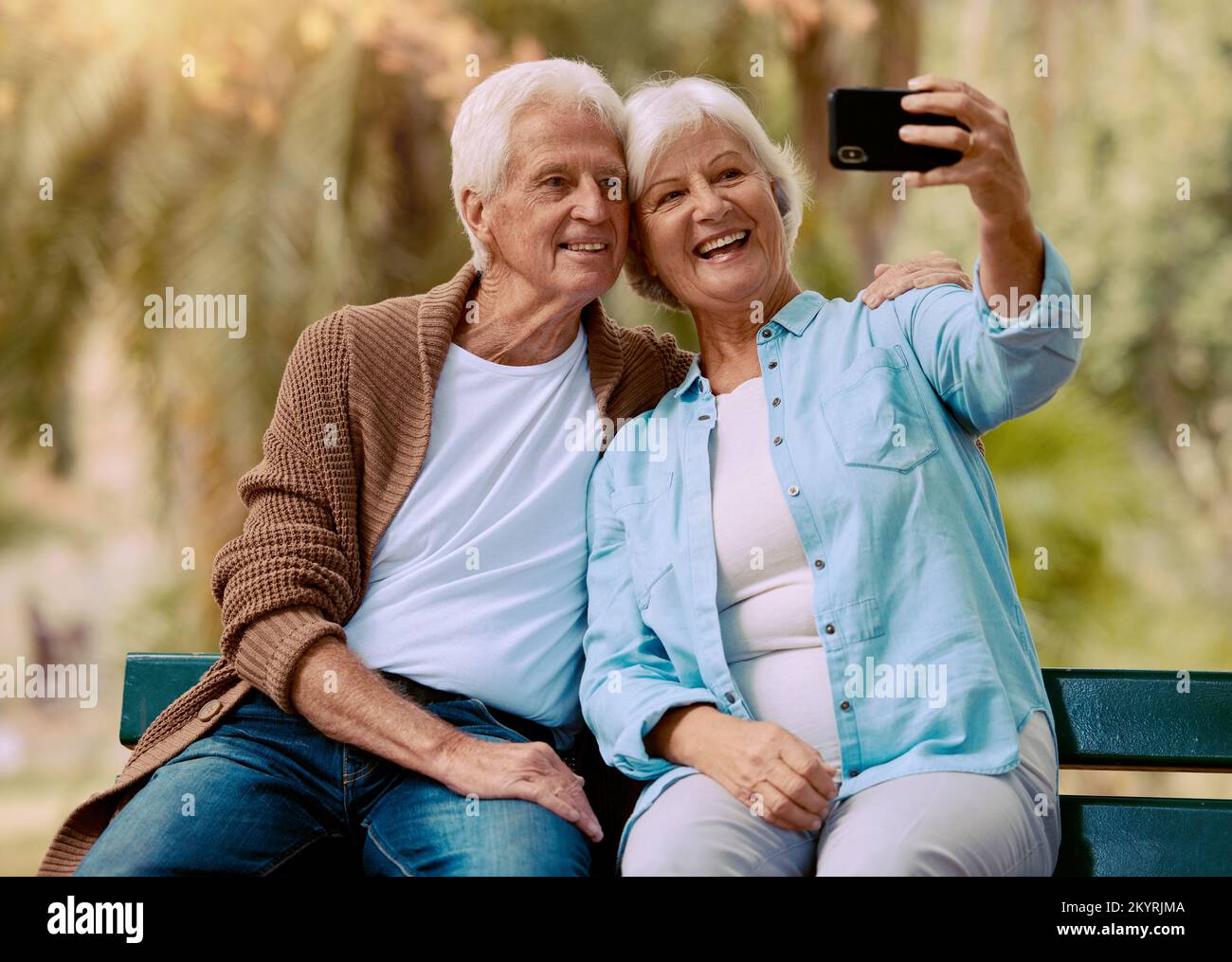 Senior couple, phone selfie and smile on park bench for love, care and social media profile picture of a happy retirement. Old man and woman outdoor Stock Photo