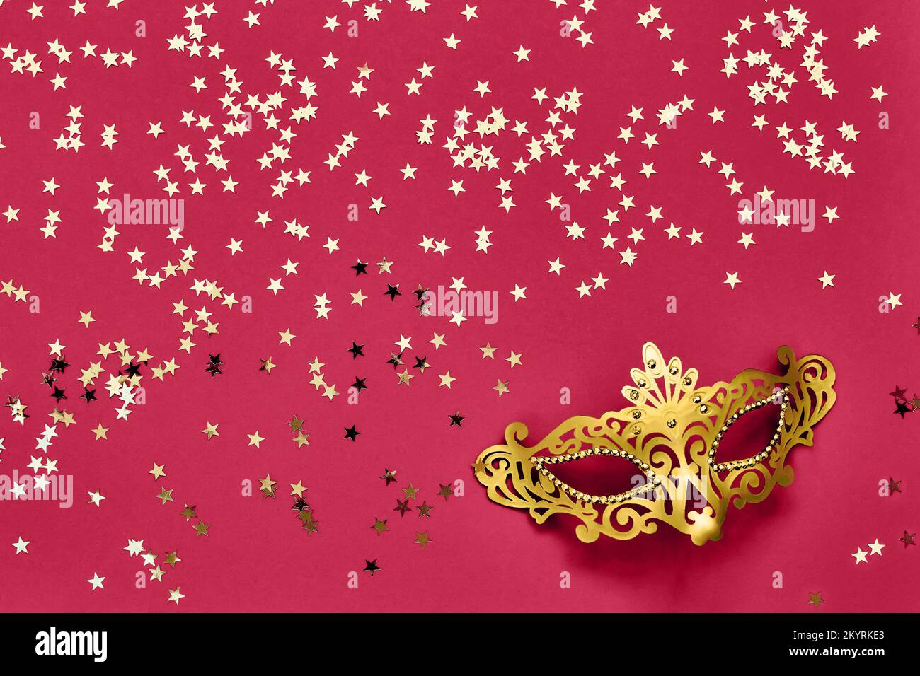 Golden carnival mask and golden stars on red viva magenta background. Top view, copy space. Carnival party celebration concept. Stock Photo