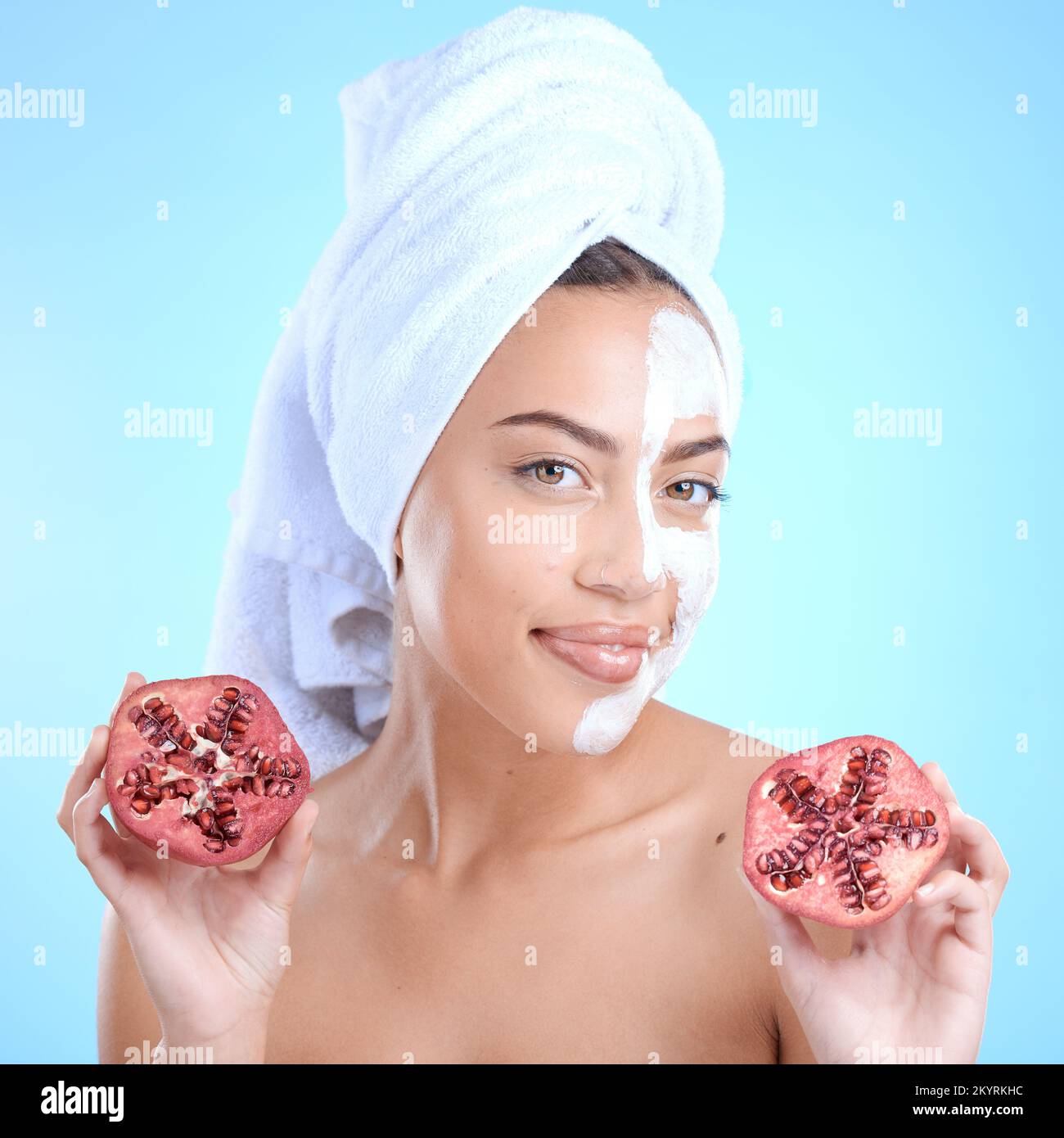 Beauty cream, face and woman with pomegranate, skincare and vitamin c for health, wellness and towel after shower in blue studio background. Model Stock Photo
