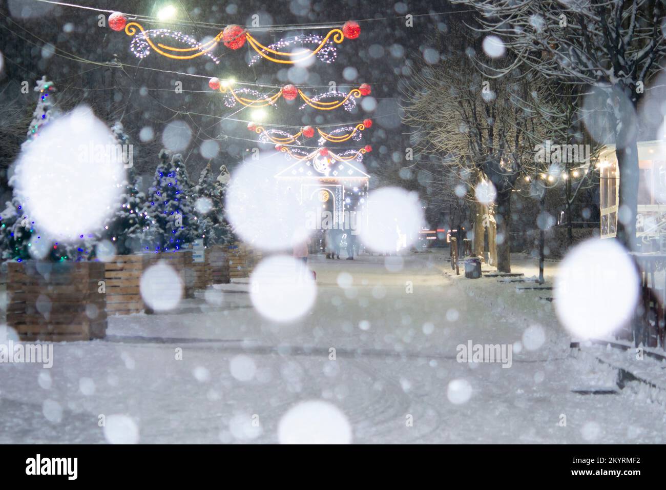 City street during snowfall at winter night. Many decorated Christmas trees, illumination, decoration on street. New Year Christmas holidays celebration. Lanterns garlands on trees Stock Photo