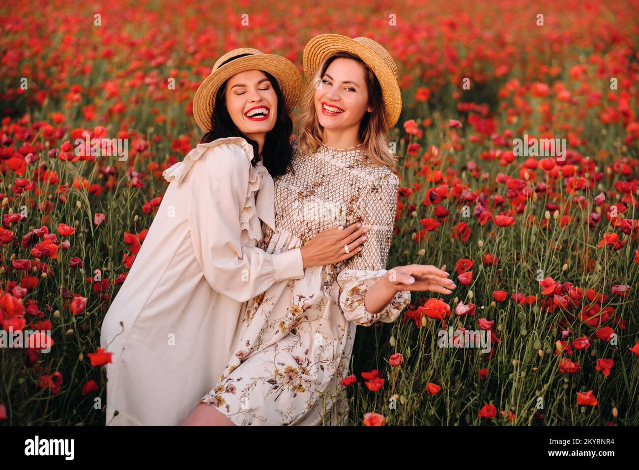 Two girlfriends in dresses and a hat in a poppy field in summer at ...