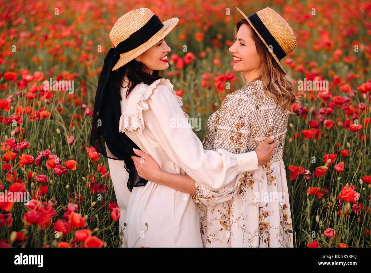 Two girlfriends in dresses and a hat in a poppy field in summer at ...