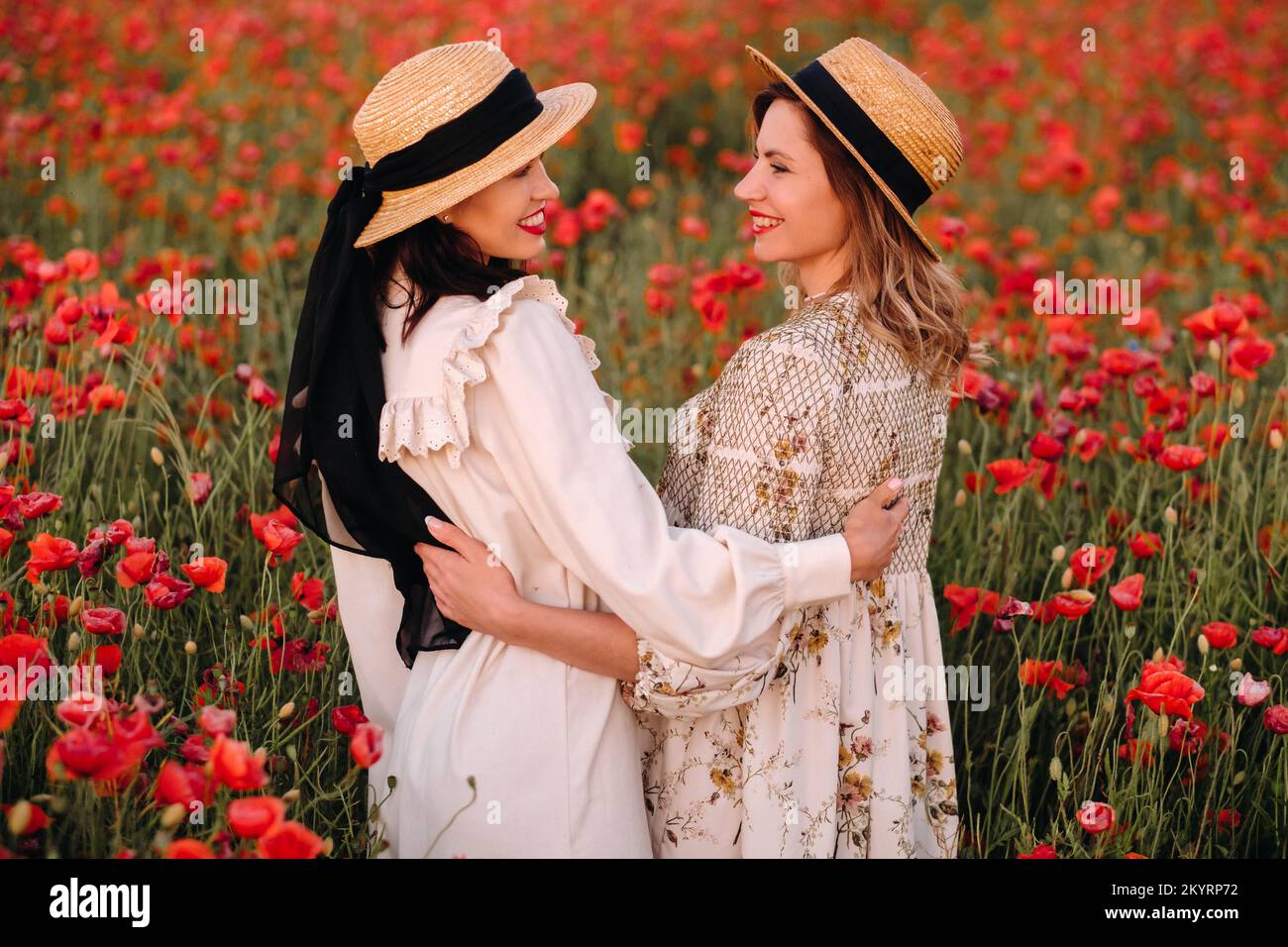 Two girlfriends in dresses and a hat in a poppy field in summer at ...