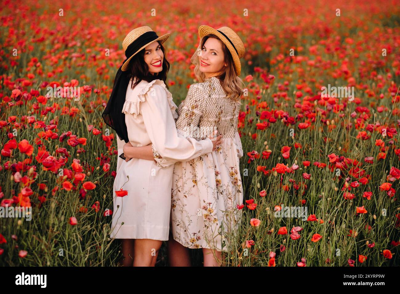 Two girlfriends in dresses and a hat in a poppy field in summer at ...