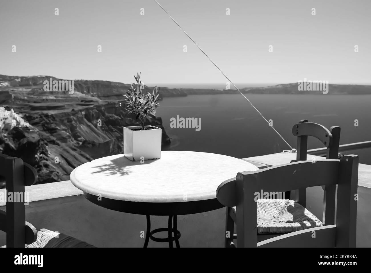 View of a small olive tree in a vase and the famous village of Fira Santorini in the background in black and white Stock Photo