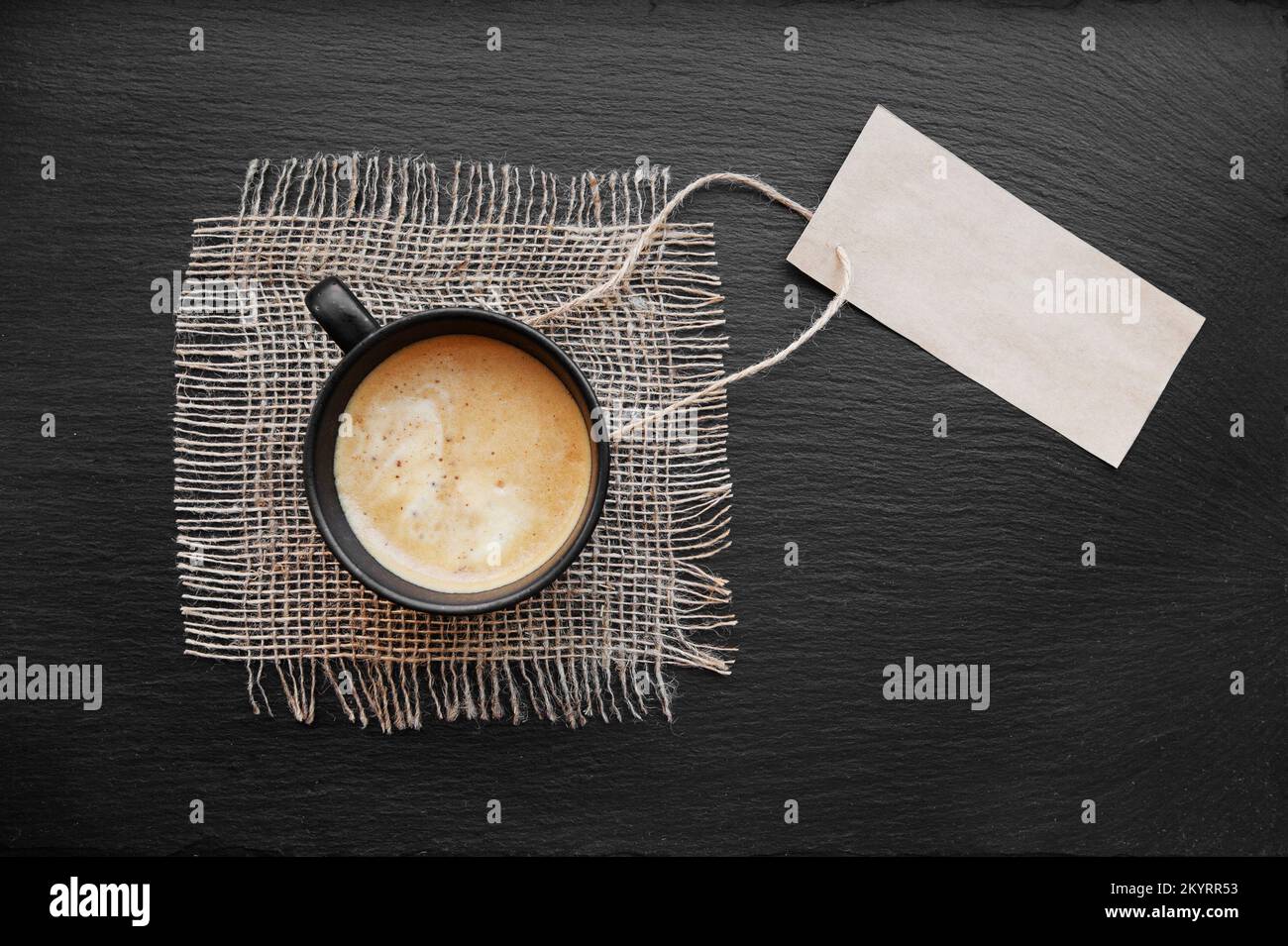 Coffee cup on rustic burlap and blank paper card. Top view with copyspace for your text. black background, cappuccino. price tag Stock Photo