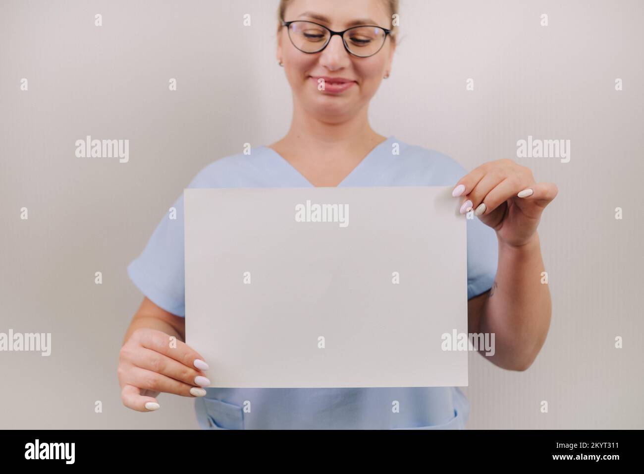 Portrait of a female doctor in a blue robe holding a white blank sheet ...