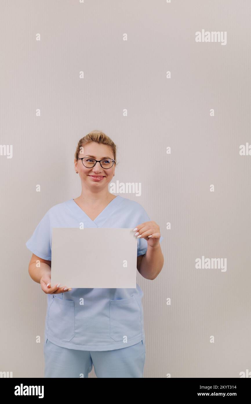 Portrait of a female doctor in a blue robe holding a white blank sheet ...