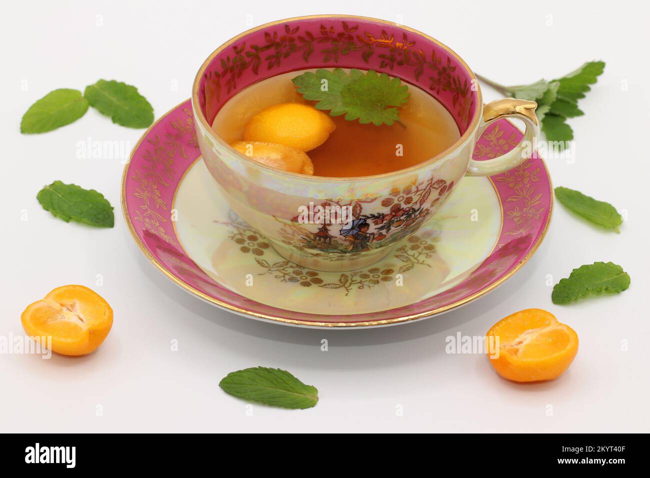 A beautiful vintage porcelain tea cup with a melissa leaf and calamansi slices. Mint leaves and calamondin fruit halves lie around.  Citrus microcarpa Stock Photo
