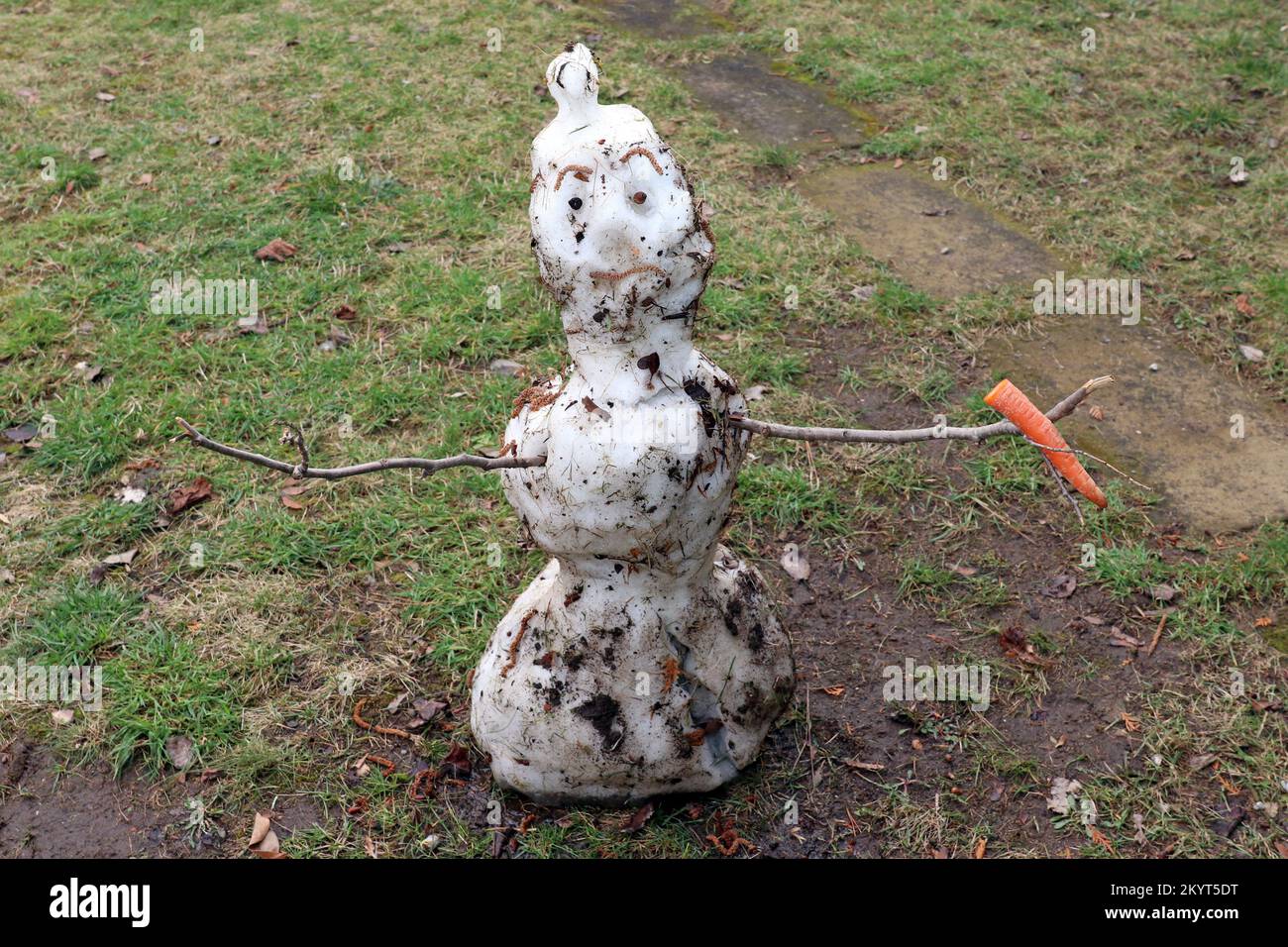 A sad snowman is melting. He holds a carrot in his hands. Too little snow in winter. Climate change. Global warming. Goodbye winter, hello spring! Stock Photo