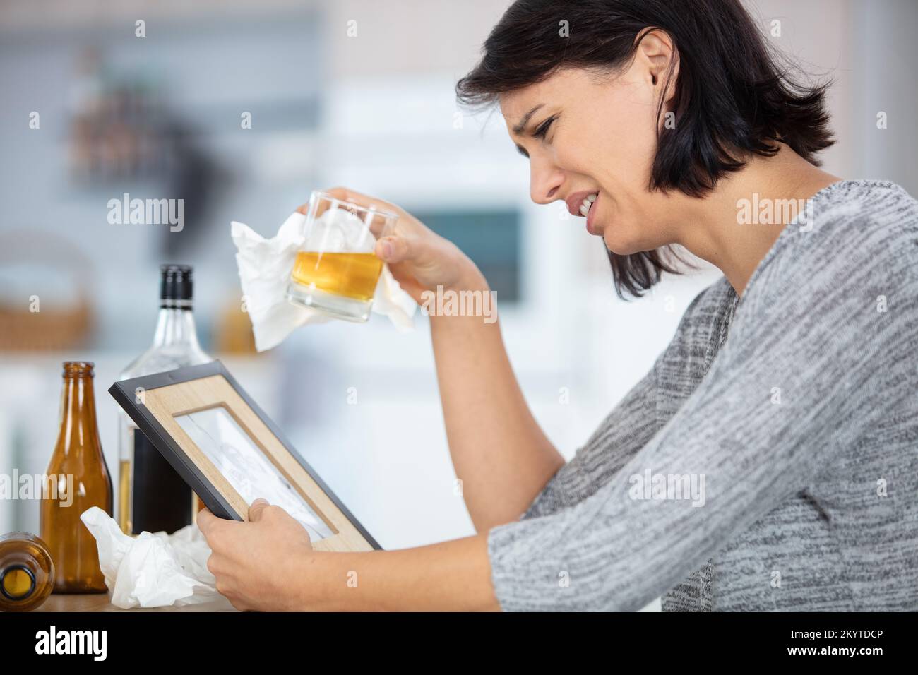 woman holding alcohol crying while looking at photograph frame Stock Photo