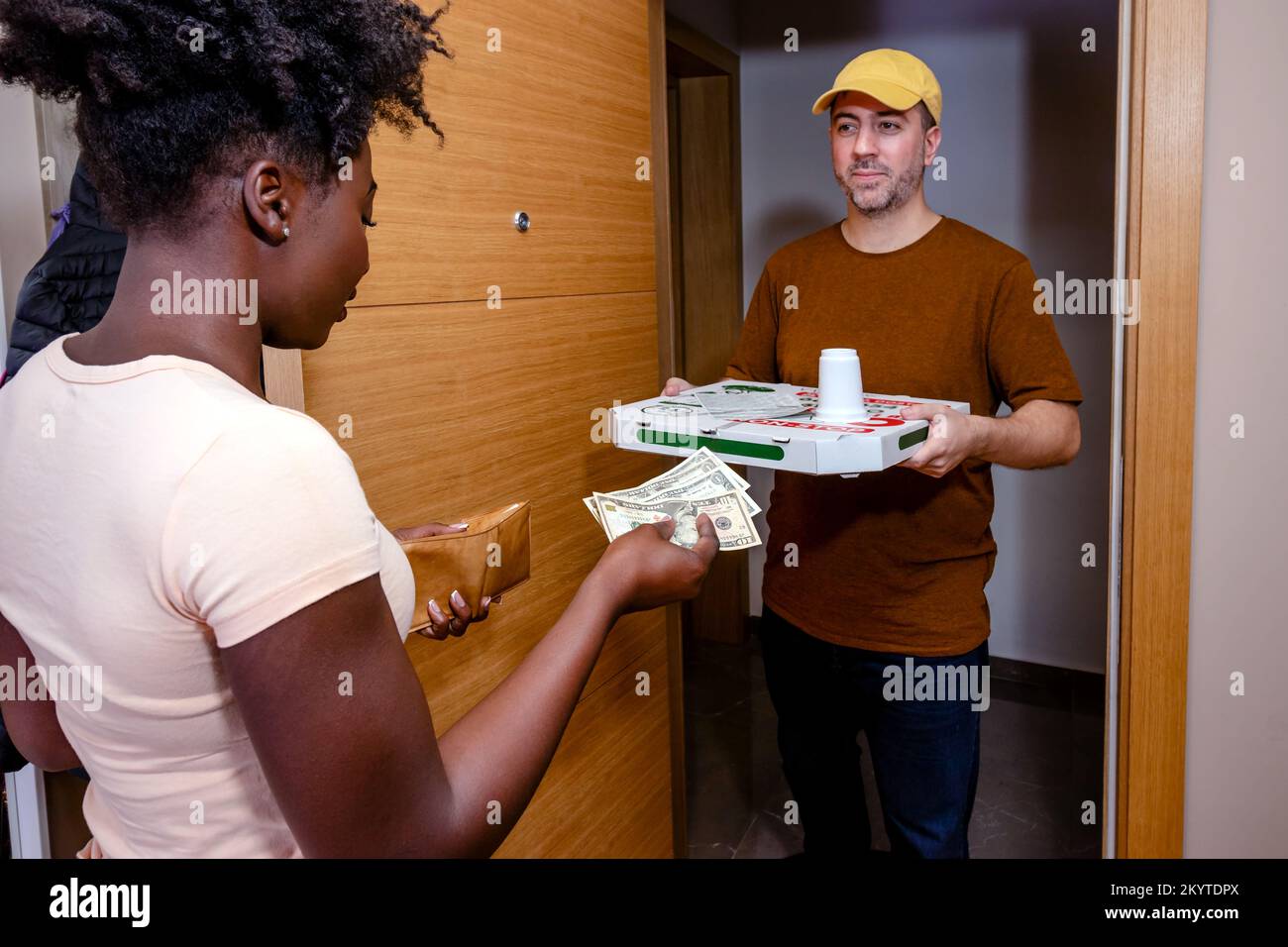 A young woman is paying for pizza delivery. Girl handing cash to a