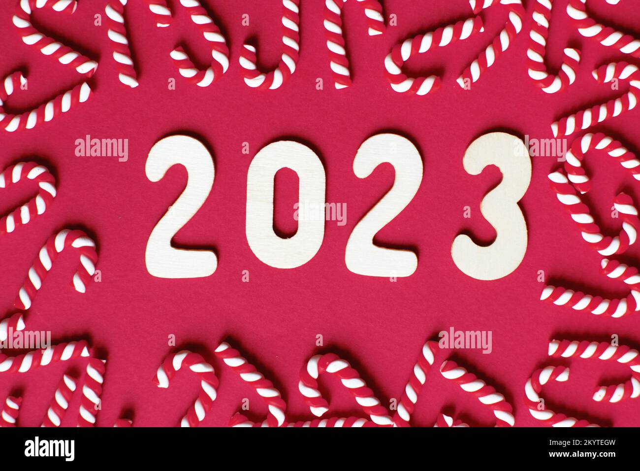 Flat lay Christmas composition with frame of candy canes and number 2023 on a red background. Copy space for text. Stock Photo
