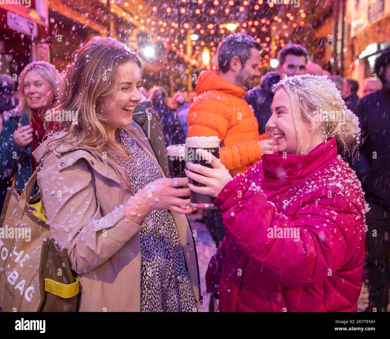 Bronagh McCarron (left) and Shannon Gillespie on the cobbled streets of Commercial Court outside the Duke of York bar in Belfast as Guinness brought its iconic Christmas ad to life with a snow machine as guests were treated to a pint to start the festive season. Stock Photo