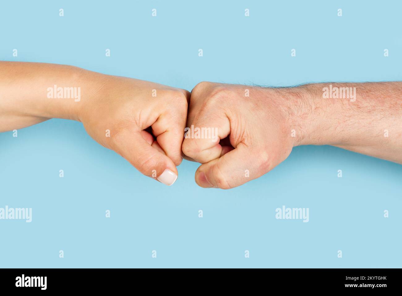 Hands of man and woman bumping fists on a light blue background with ...