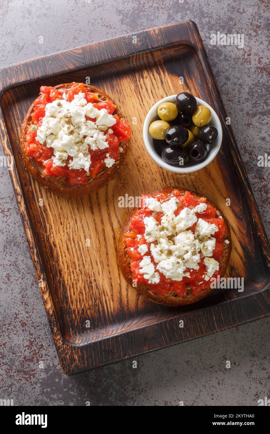 Traditional meze or a light meal on the island of Crete, dakos is often called Greek bruschetta closeup on the wooden board on the table. Vertical top Stock Photo