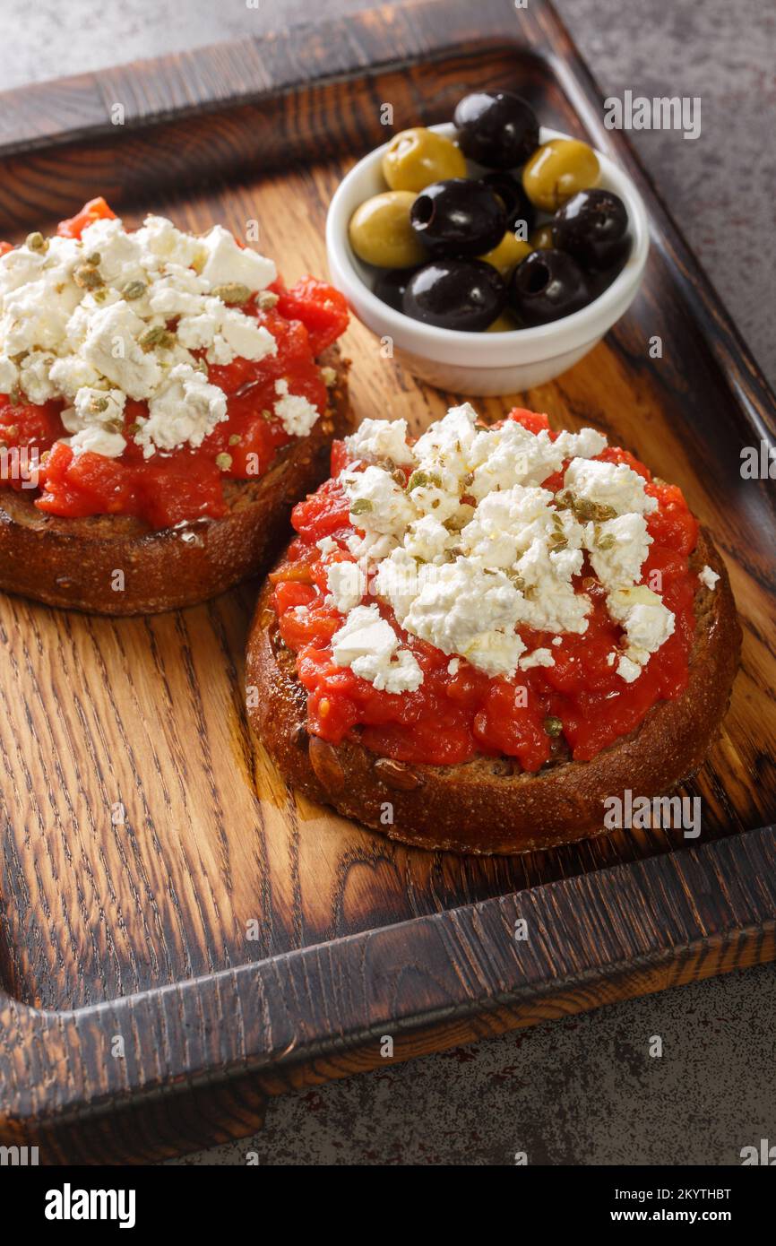 Traditional meze or a light meal on the island of Crete, dakos is often called Greek bruschetta closeup on the wooden board on the table. Vertical Stock Photo