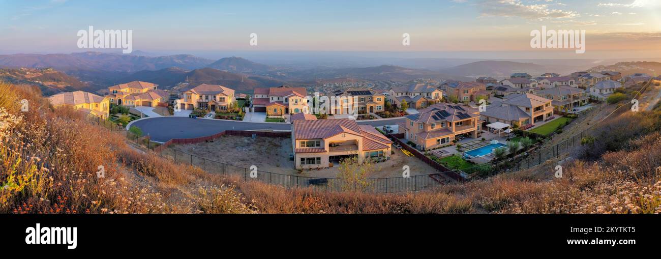 View of a fenced residential area at San Diego, California. Large houses on a cul de sac road against the view of mountains and sky at the background. Stock Photo