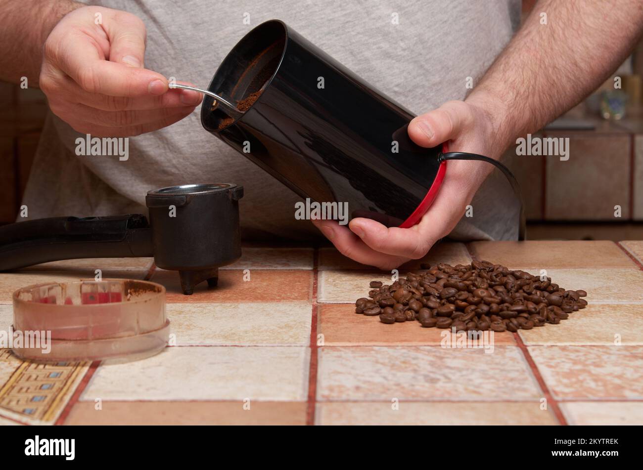 Preparation of coffee: male hands pour ground coffee into the horn of the coffee maker. Coffee beans, an electric coffee grinder, and a white cup and Stock Photo