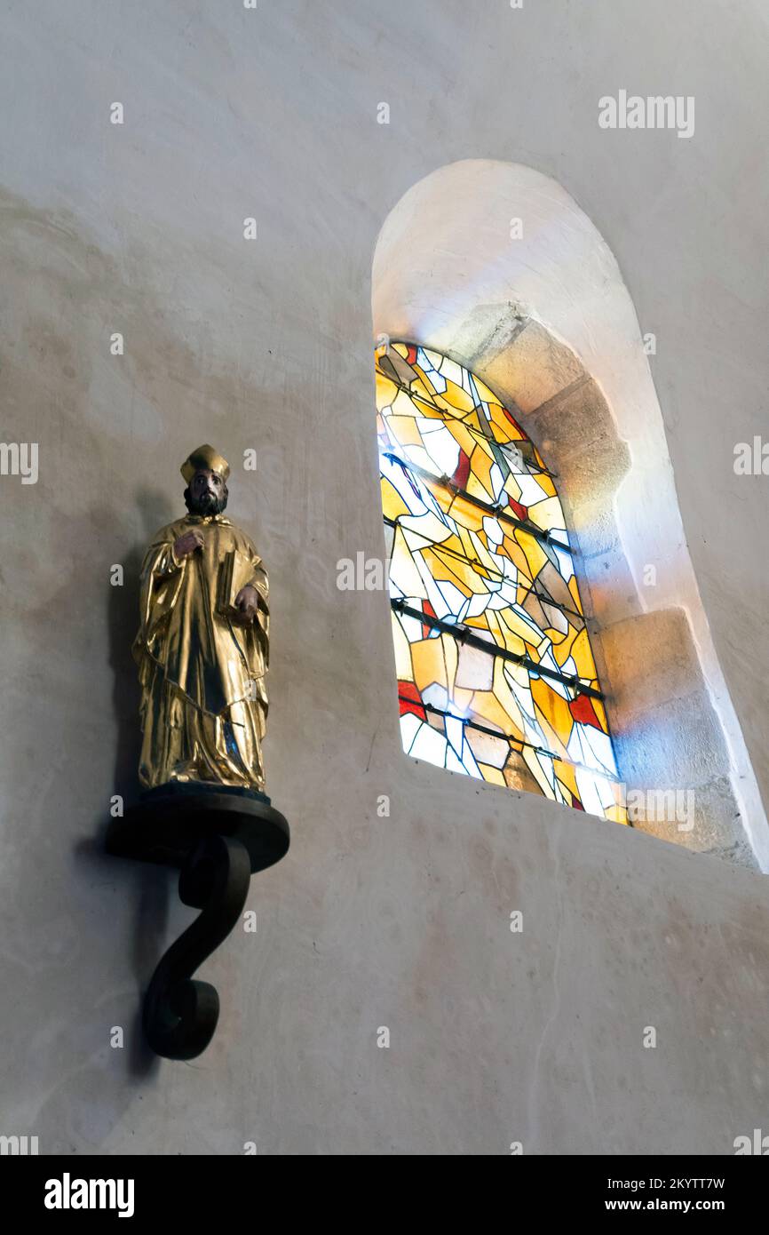 Religious statue on a wall under a stained glass window. France Stock Photo