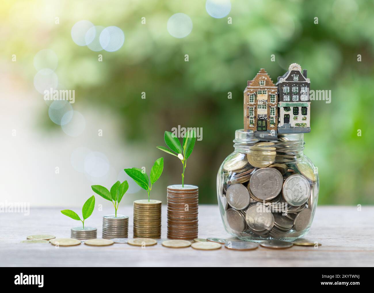 House toy on coin in jar and coin stact with plant growth on top concept of saving money for house. Out of focus background. Stock Photo