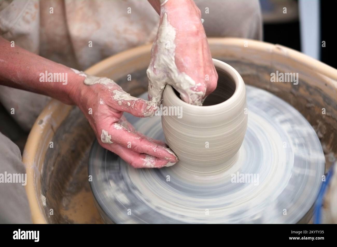 Potter sat to left of spinning potter's wheel with two hands making