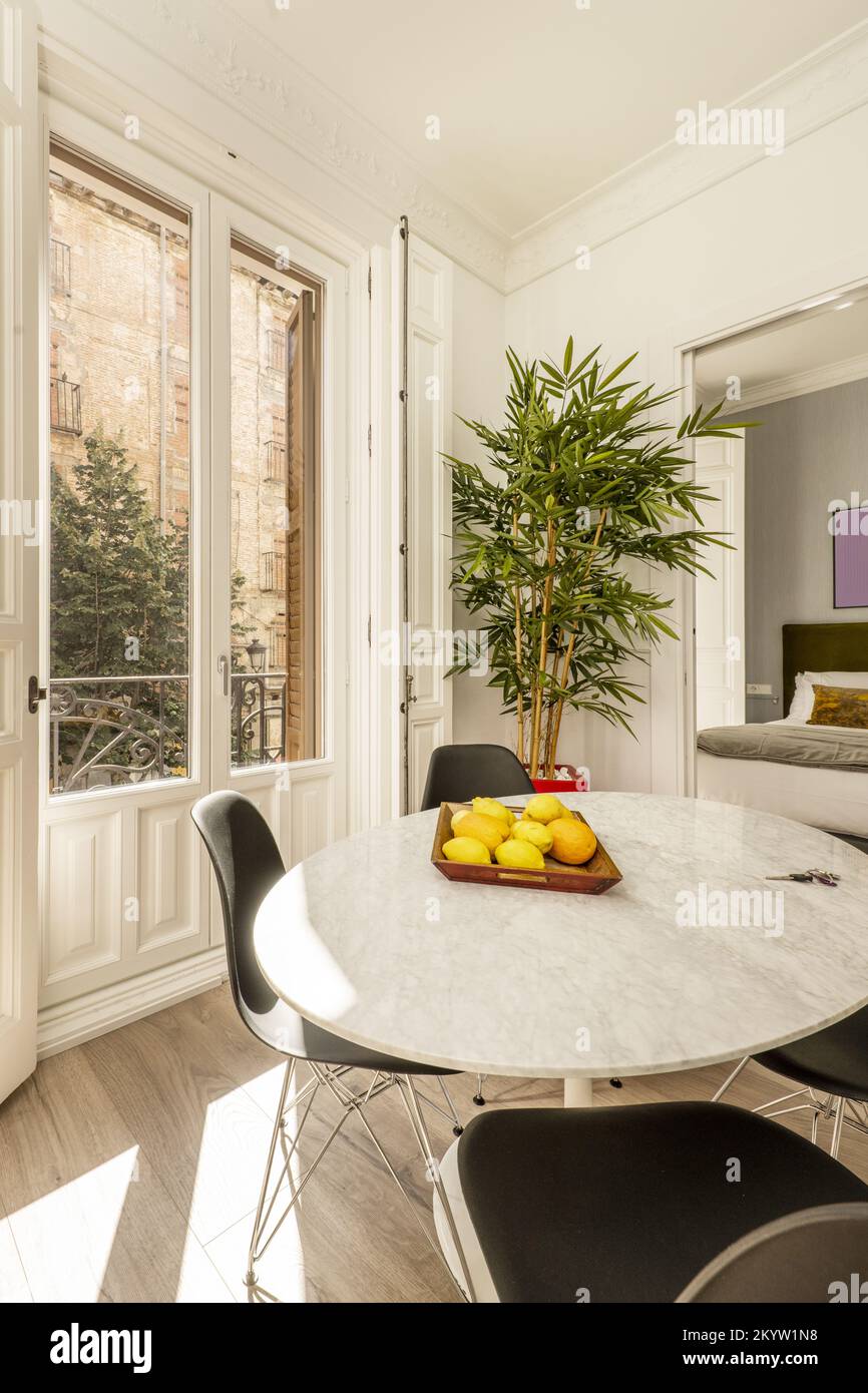 Living room with circular white marble table next to a balcony with white lacquered wooden doors Stock Photo