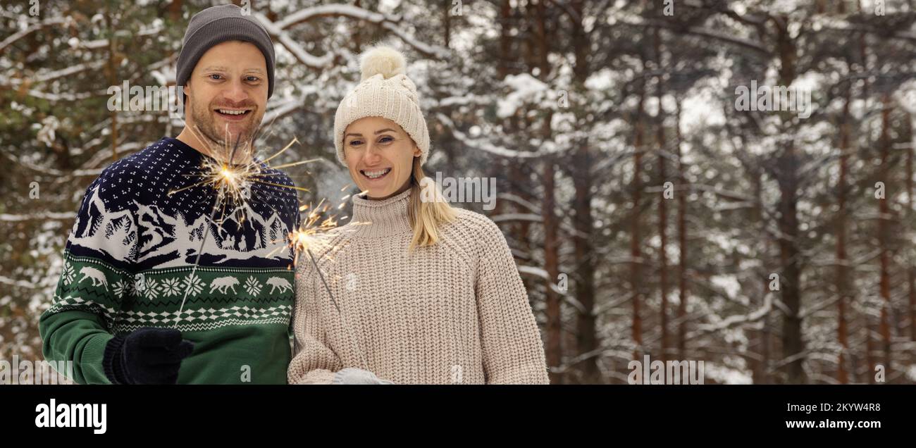 young couple with sparklers in snowy winter forest. people with burning bengal lights outdoors. banner with copy space Stock Photo
