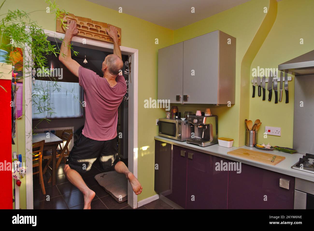 Man strength training at home using a fingerboard in his kitchen. Stock Photo