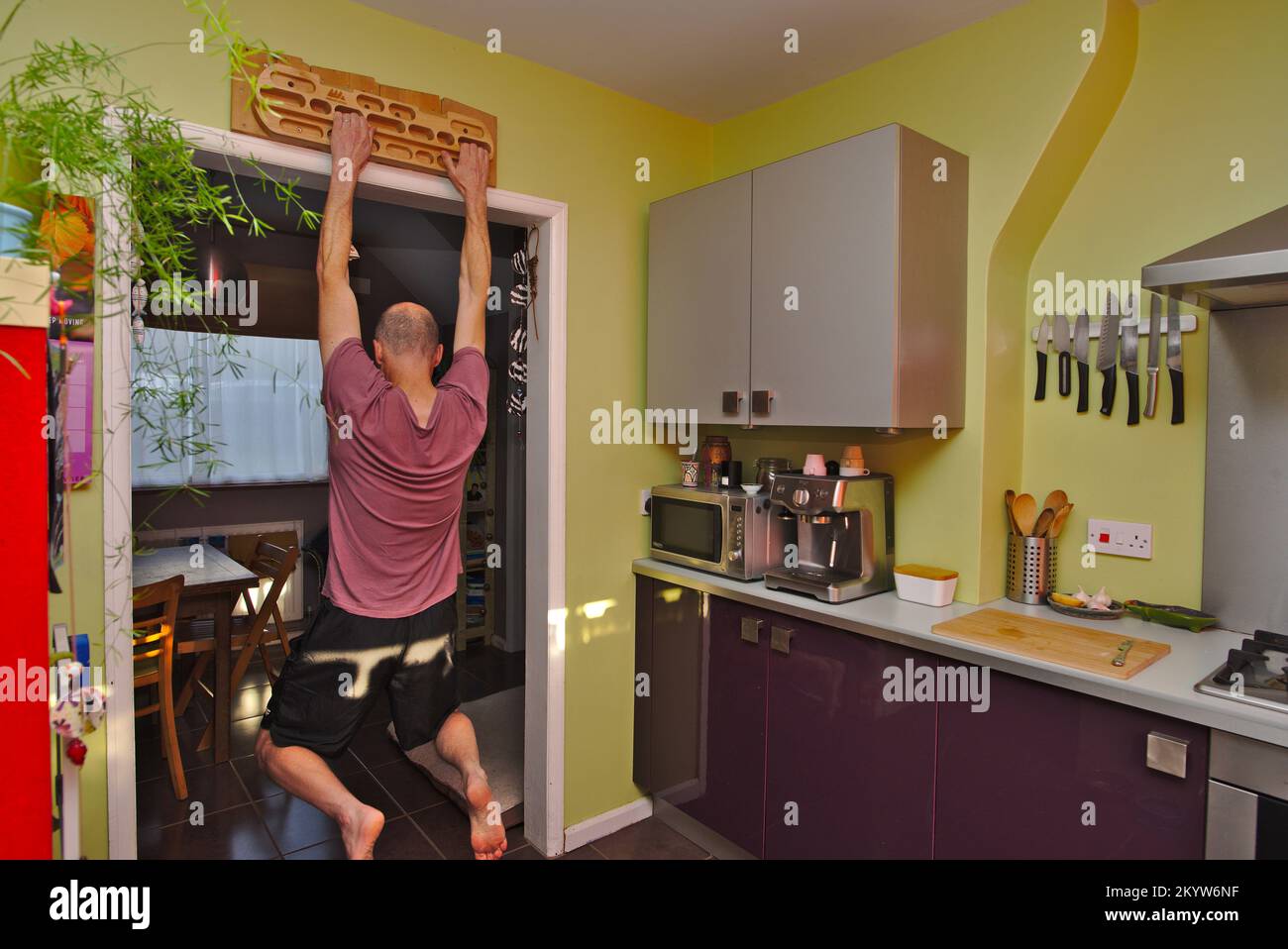 Man strength training at home using a hangboard in his kitchen. Stock Photo
