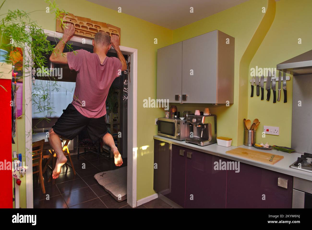 Man strength training at home using a fingerboard in his kitchen. Stock Photo