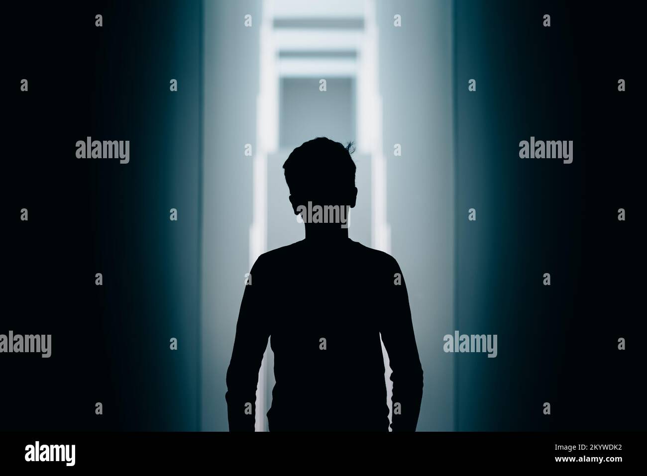An anonymous and abstract silhouette of a young male person in front of an impressively lit staircase. Stock Photo