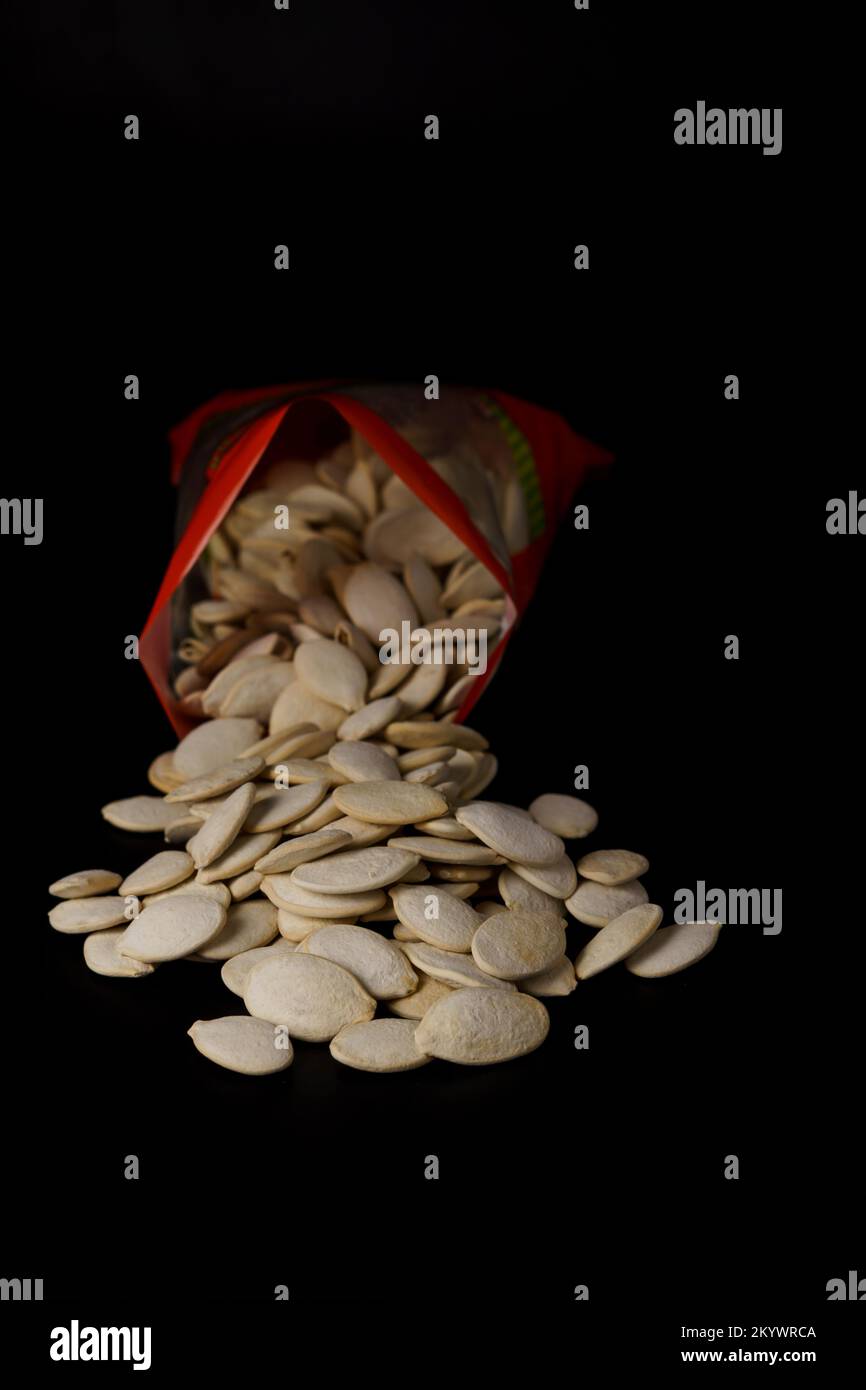 roasted pumpkin seeds coming out of their red bag on a black table Stock Photo