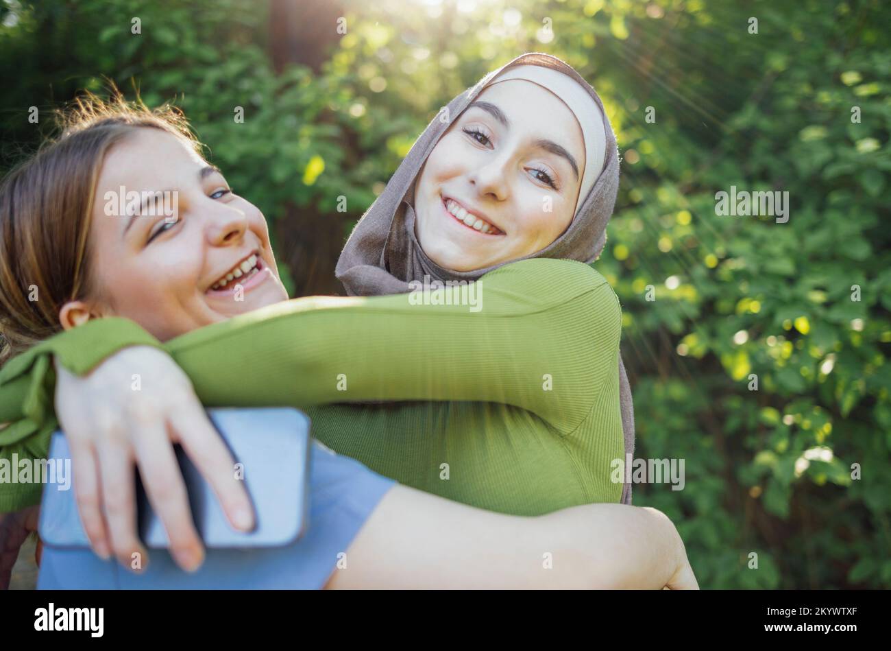 Strong female friendship. Happy two teen girls best friends holding hands and hugging while standing in front of park. Multiethnical friends Stock Photo