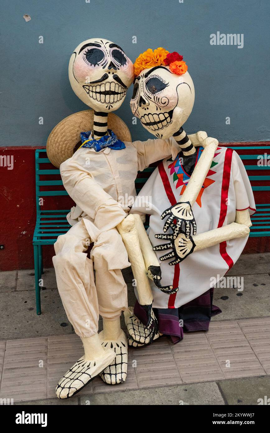 A couple of papier mache skeletons in indigenous dress celebrate Day of the Dead on a bench on a street in Oaxaca, Mexico. Stock Photo