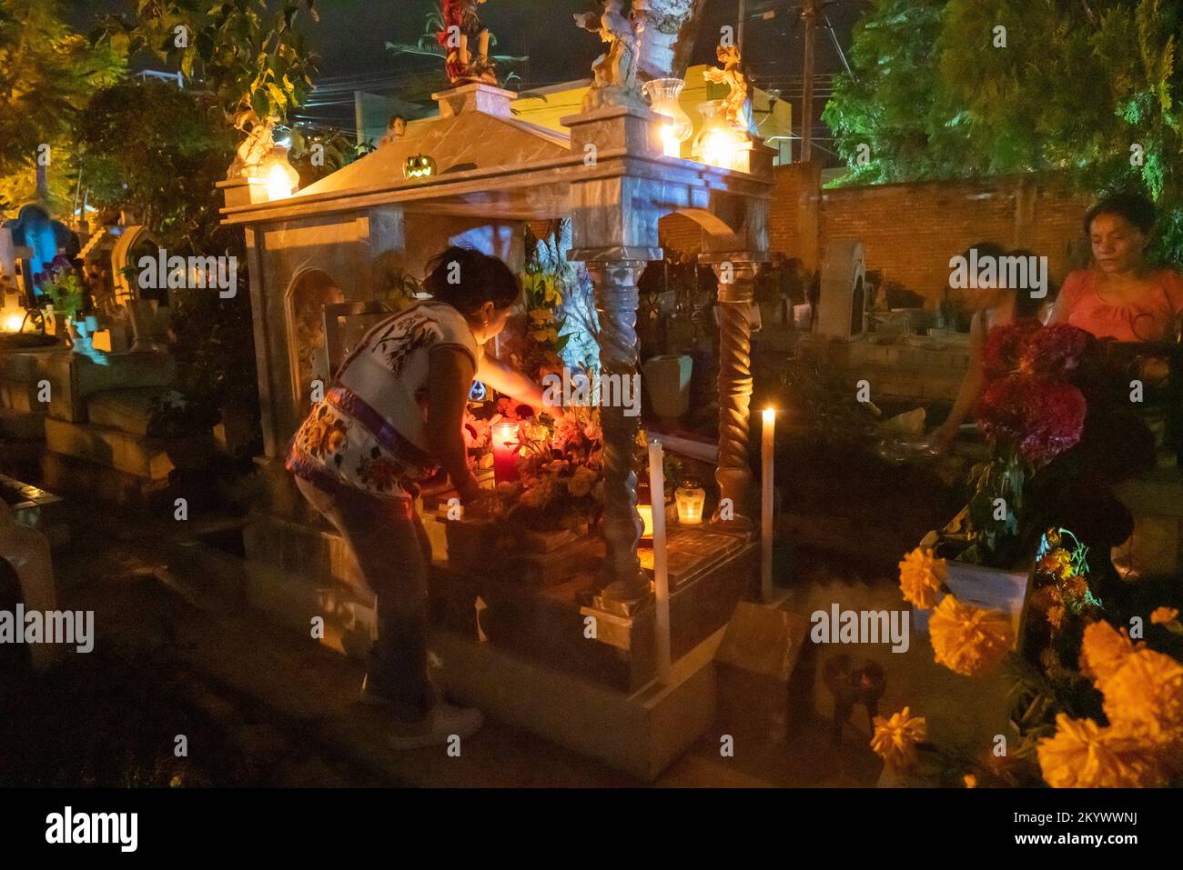 A woman decorates a grave in the Xochimilco Cemetery for the Day of the Dead or Dia de los Muertos in Oaxaca, Mexico. Stock Photo