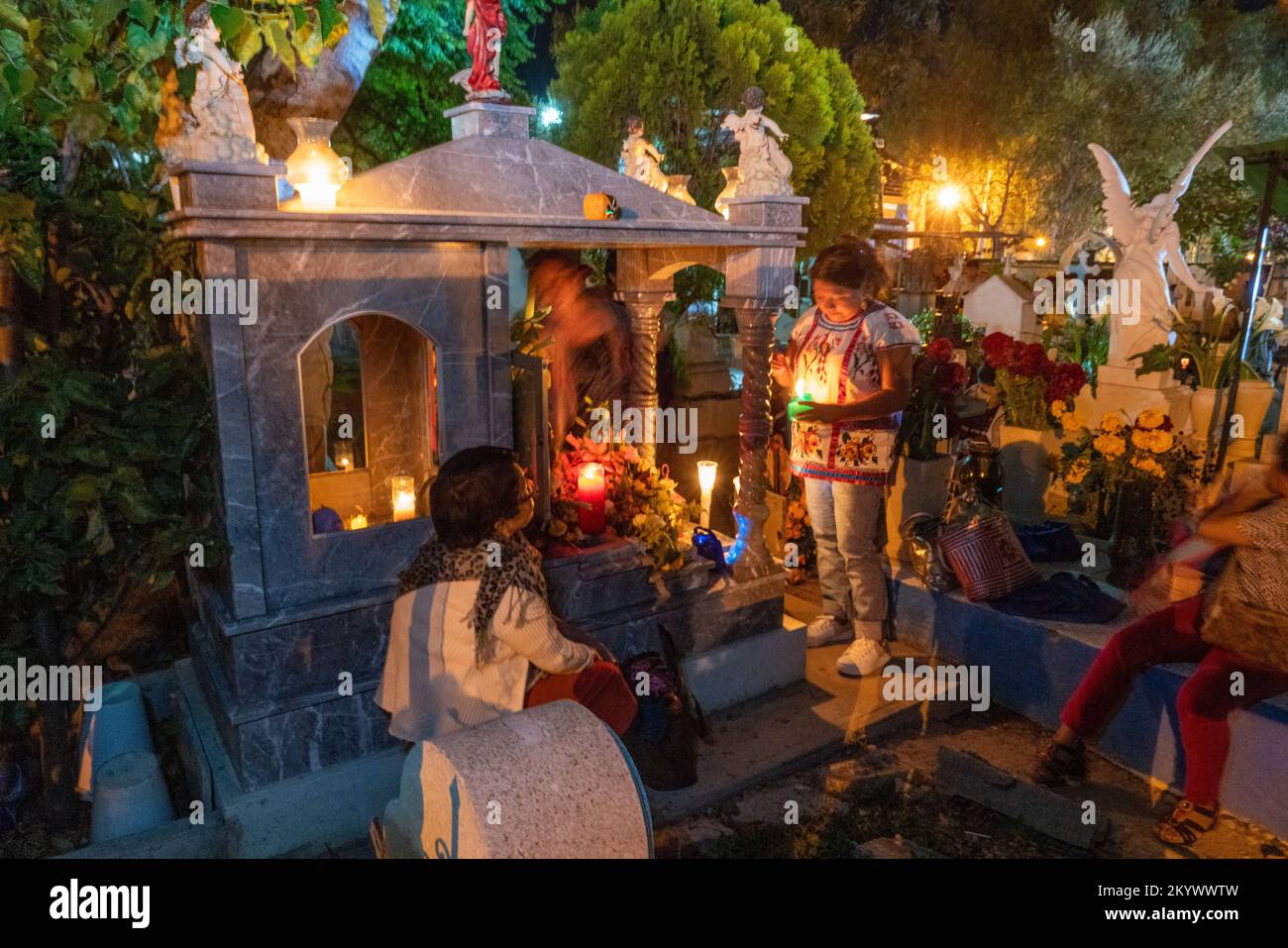 Women sit by a grave in the Xochimilco Cemetery decorated for the Day of the Dead or Dia de los Muertos in Oaxaca, Mexico. Stock Photo
