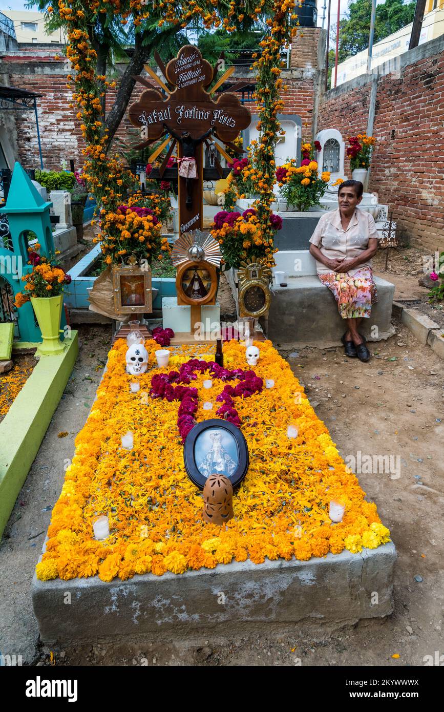 A woman sits by a grave in the Xochimilco Cemetery decorated for the Day of the Dead or Dia de los Muertos in Oaxaca, Mexico. Stock Photo