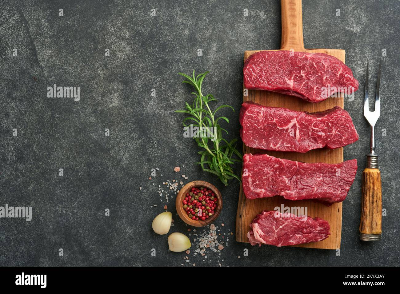Raw steaks. Top blade steaks on wood burning board with spices, rosemary, vegetables and ingredients for cooking on black background. Top view.  Copy Stock Photo
