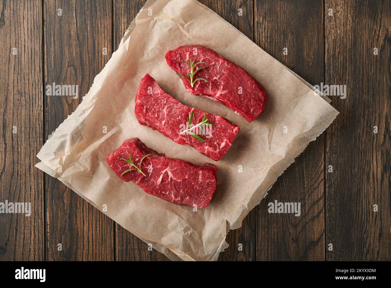 Raw steaks. Top blade steaks on wood burning board with spices, rosemary, vegetables and ingredients for cooking on old wooden background. Top view. Stock Photo