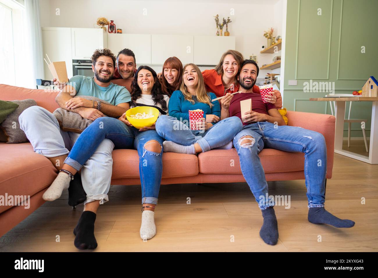 Group of roommates watching tv and eating snack sitting on the couch - Cheerful young students having fun in living room Stock Photo