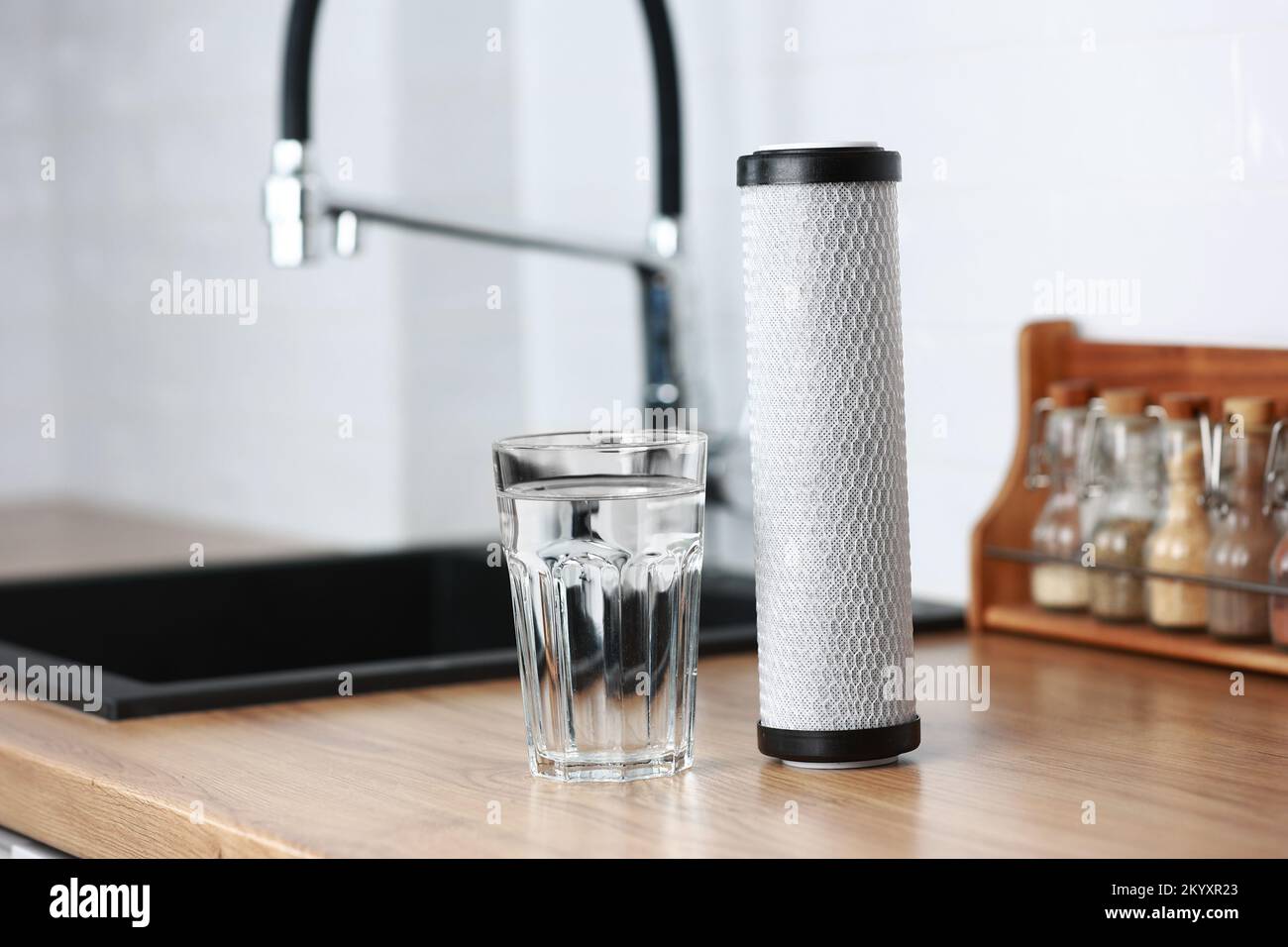 A glass of clean fresh water and carbon filter cartridge on wooden ...