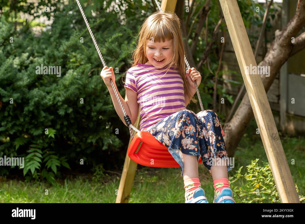 Happy girl elementary school age child sitting swinging on an simple