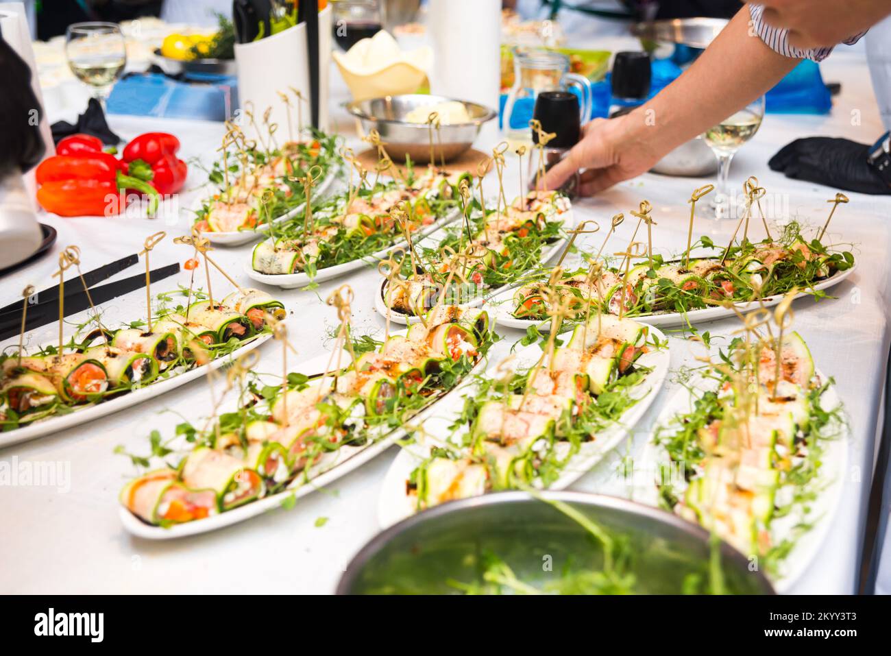 Salted trout rolls with zucchini, cottage cheese and a bouquet of micro herbs. Lots of long plates at the banquet. Stock Photo