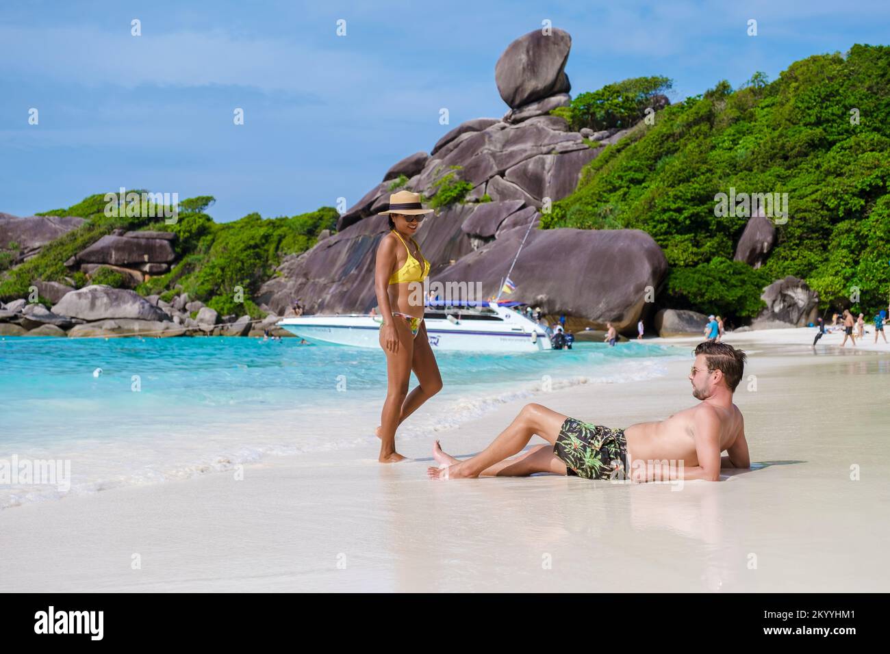 Asian Thai women and Caucasian men on the beach of the Similan Islands in Thailand with turqouse colored ocean and white sand.  Stock Photo
