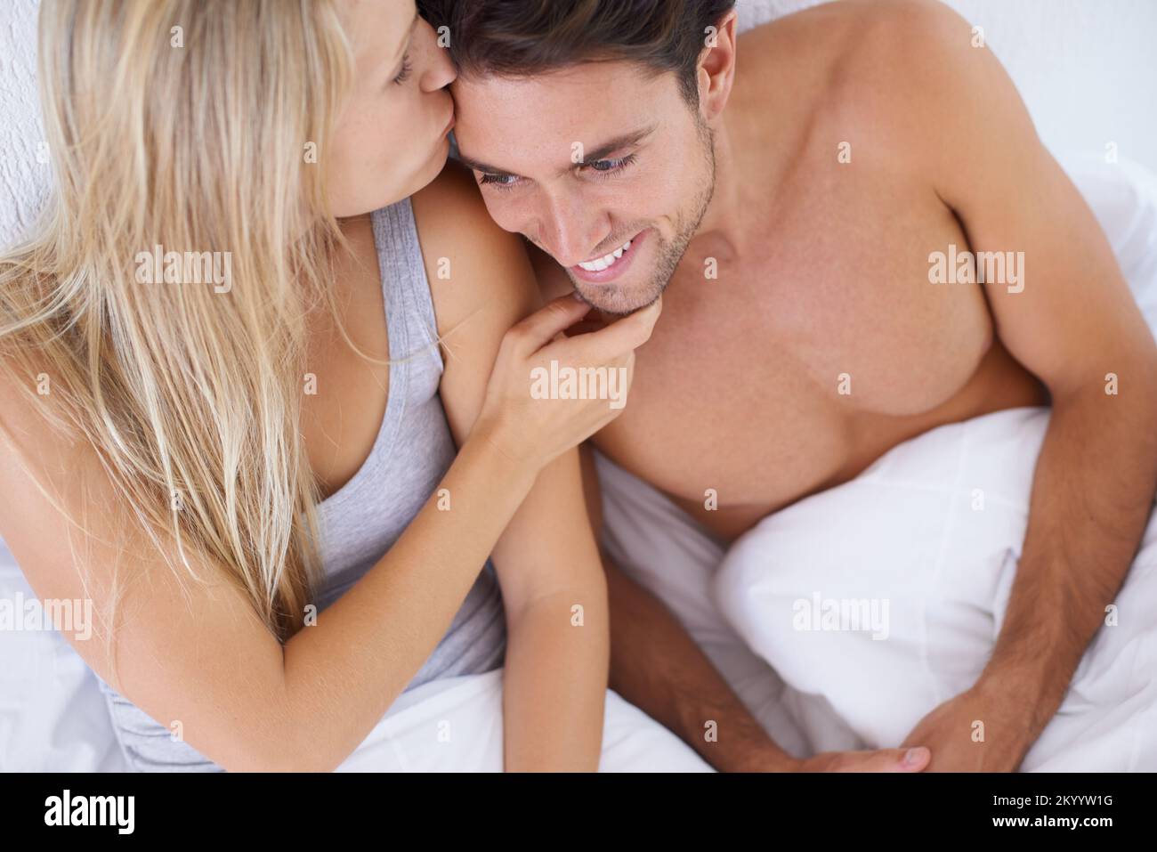 Showing her affection. A couple lying in bed together cuddling and kissing affectionately. Stock Photo