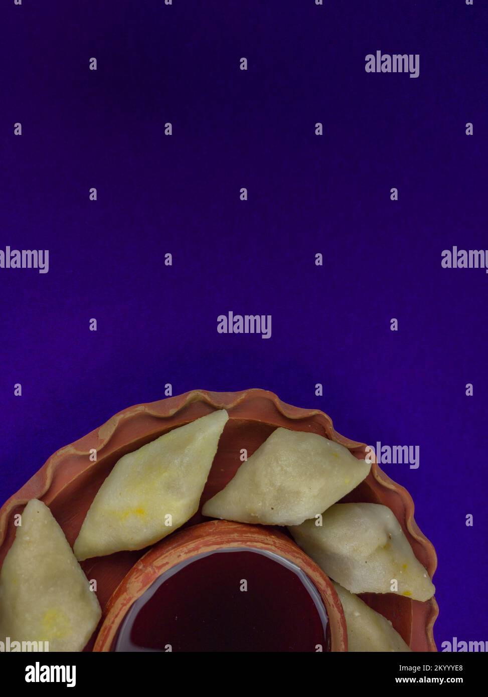 puli pithe or bengali rice flour dumplings with coconut fillings served on a clay plate with jaggery. shot against blue background.this traditional di Stock Photo